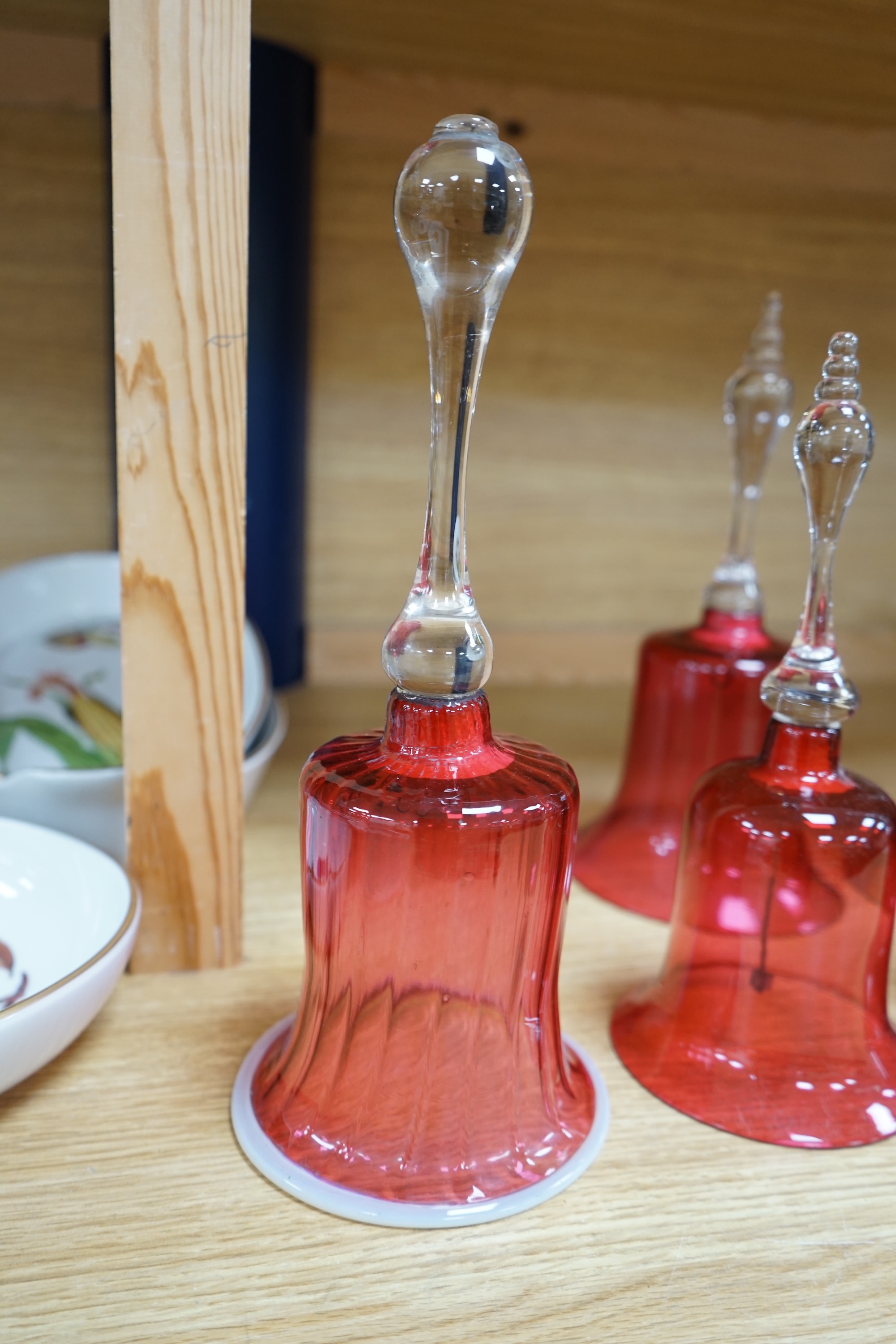 Seven 19th century cranberry glass hand bells, various sizes, largest 30.5cm high. Condition - fair